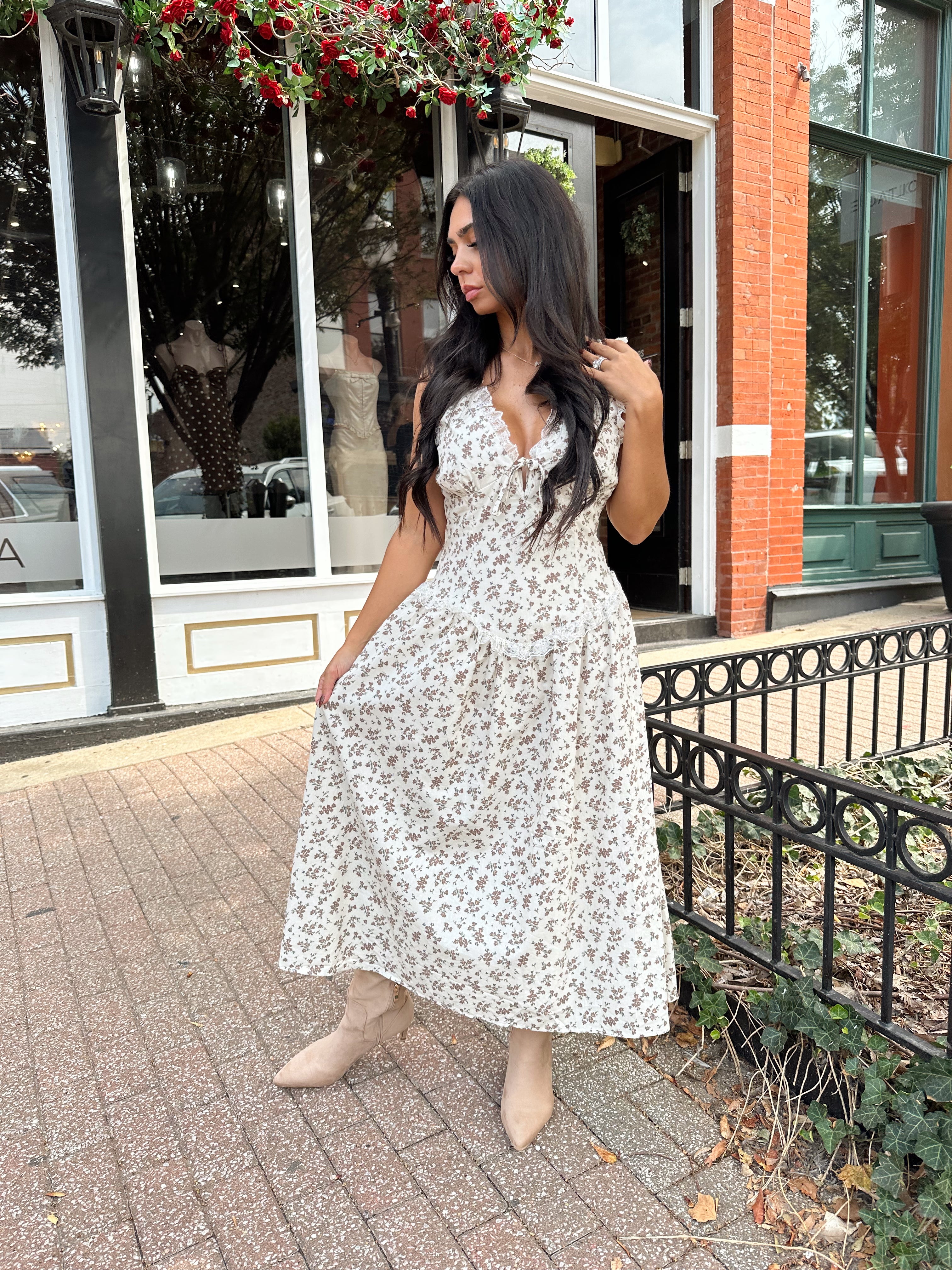 Woman wearing oatmeal midi dress with floral pattern and ruffle detail.