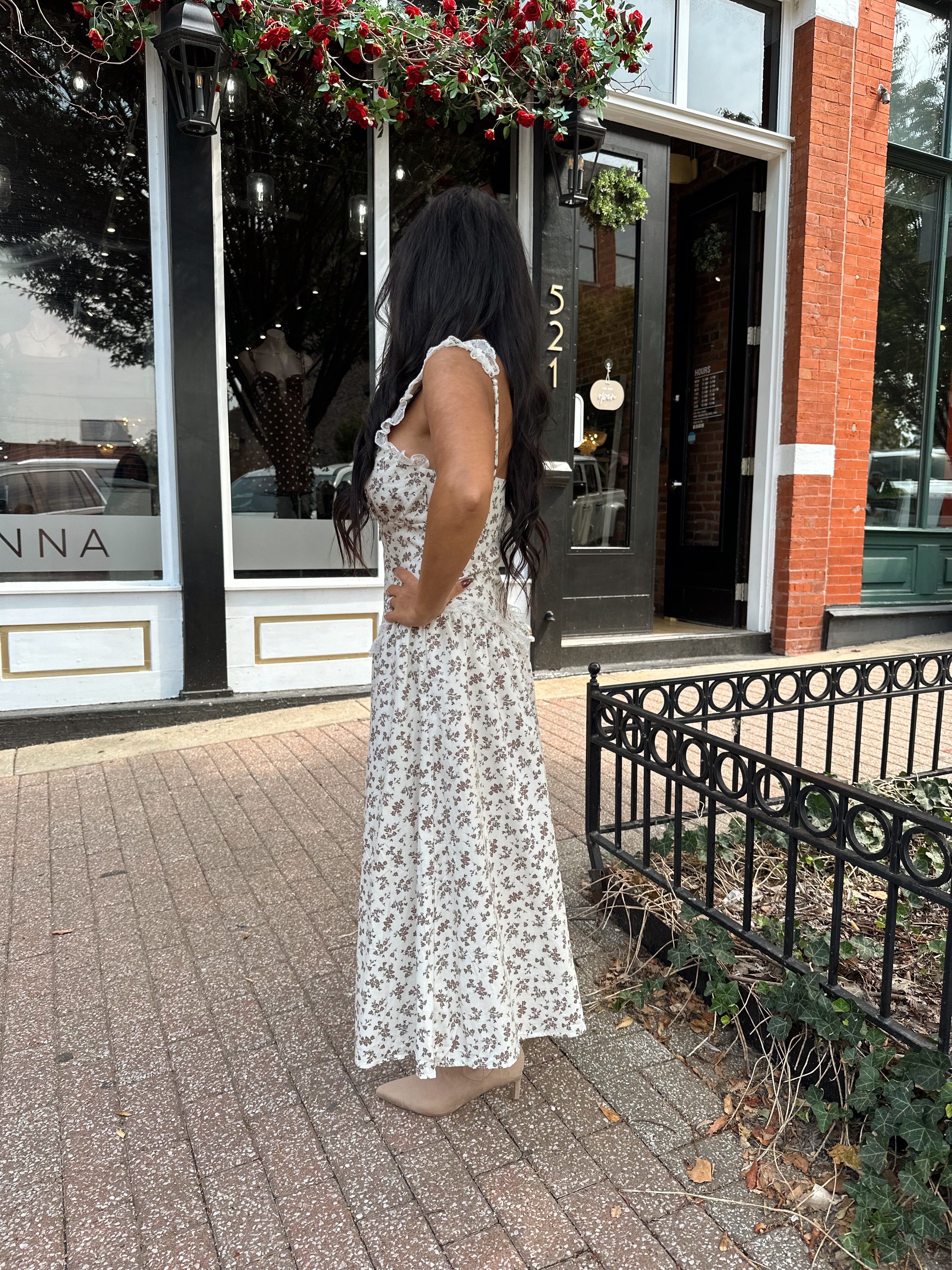Woman wearing oatmeal midi dress with floral pattern and ruffle detail.