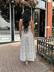 Woman wearing oatmeal midi dress with floral pattern and ruffle detail.