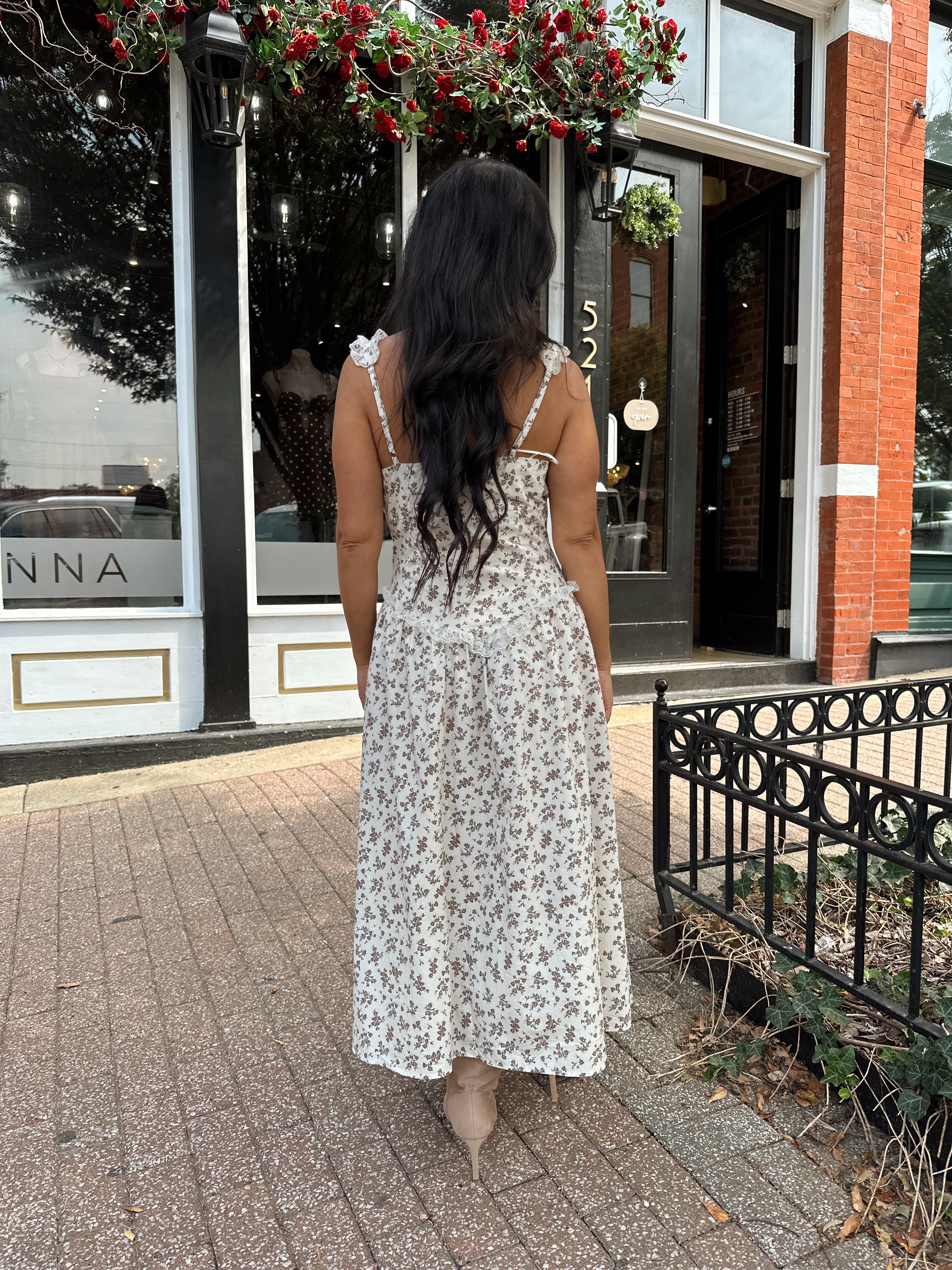 Woman wearing oatmeal midi dress with floral pattern and ruffle detail.
