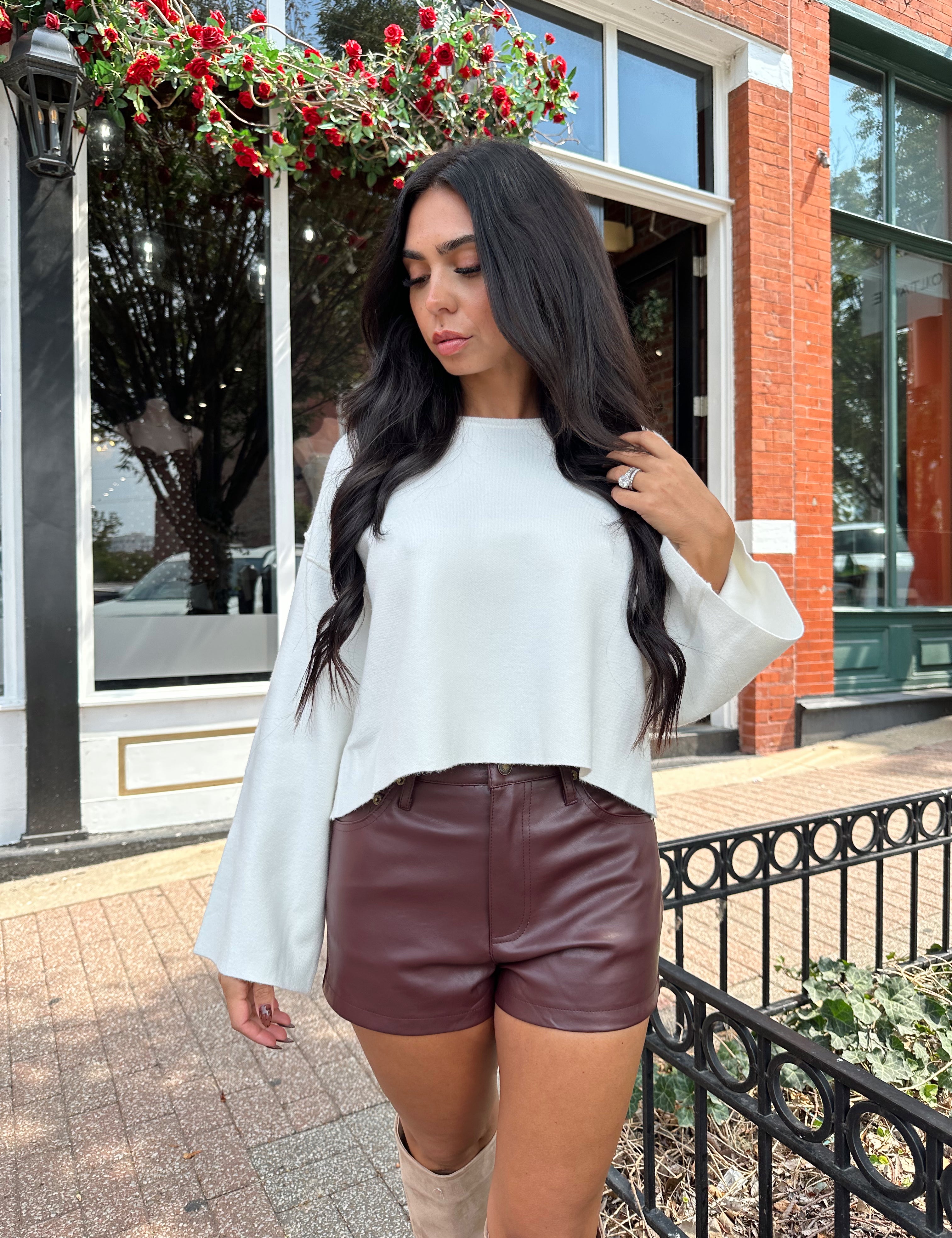 Woman wearing off white knit long sleeve sweater top with burgundy leather short.
