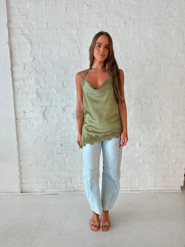 Woman wearing sage green satin lace trim top with asymmetrical hem, and open back. 