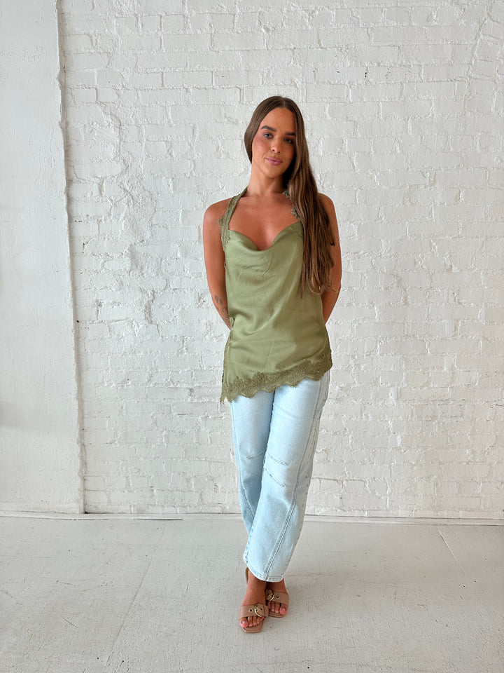 Woman wearing sage green satin lace trim top with asymmetrical hem, and open back. 