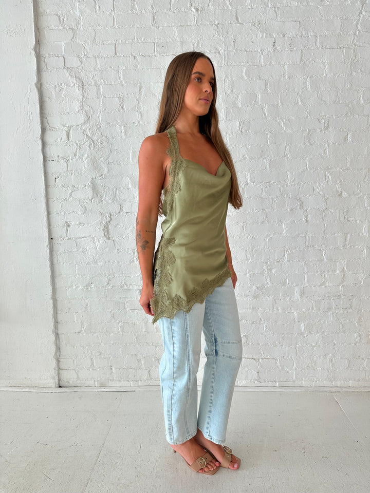 Woman wearing sage green satin lace trim top with asymmetrical hem, and open back. 