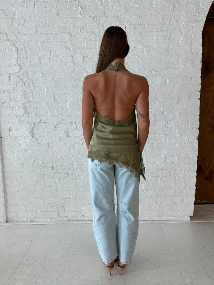 Woman wearing sage green satin lace trim top with asymmetrical hem, and open back. 