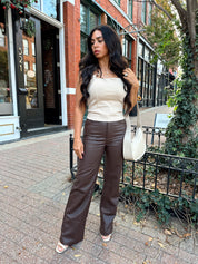 Woman wearing taupe halter neck top with chain link detail, and brown leather pant.