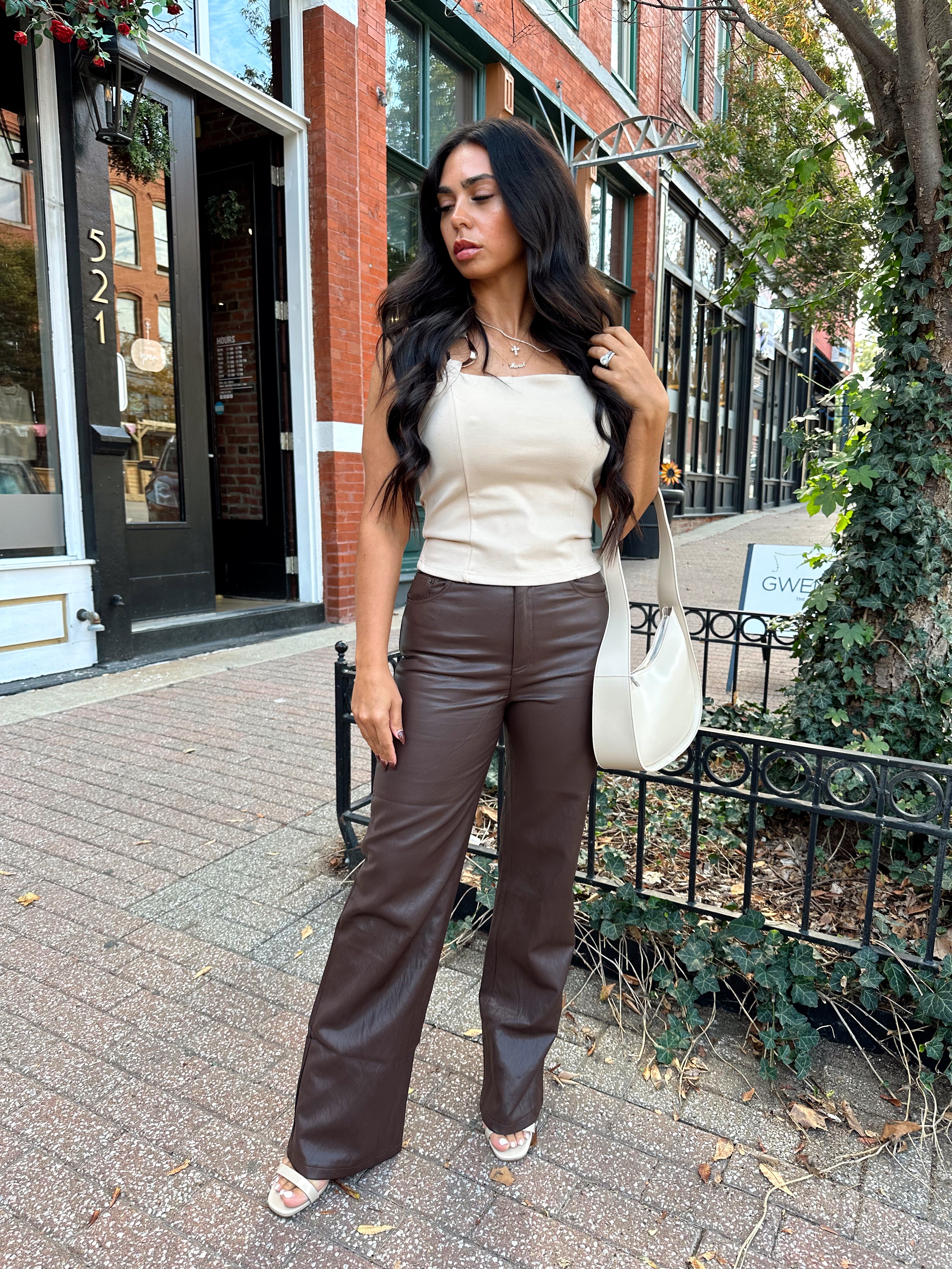 Woman wearing taupe halter neck top with chain link detail, and brown leather pant.