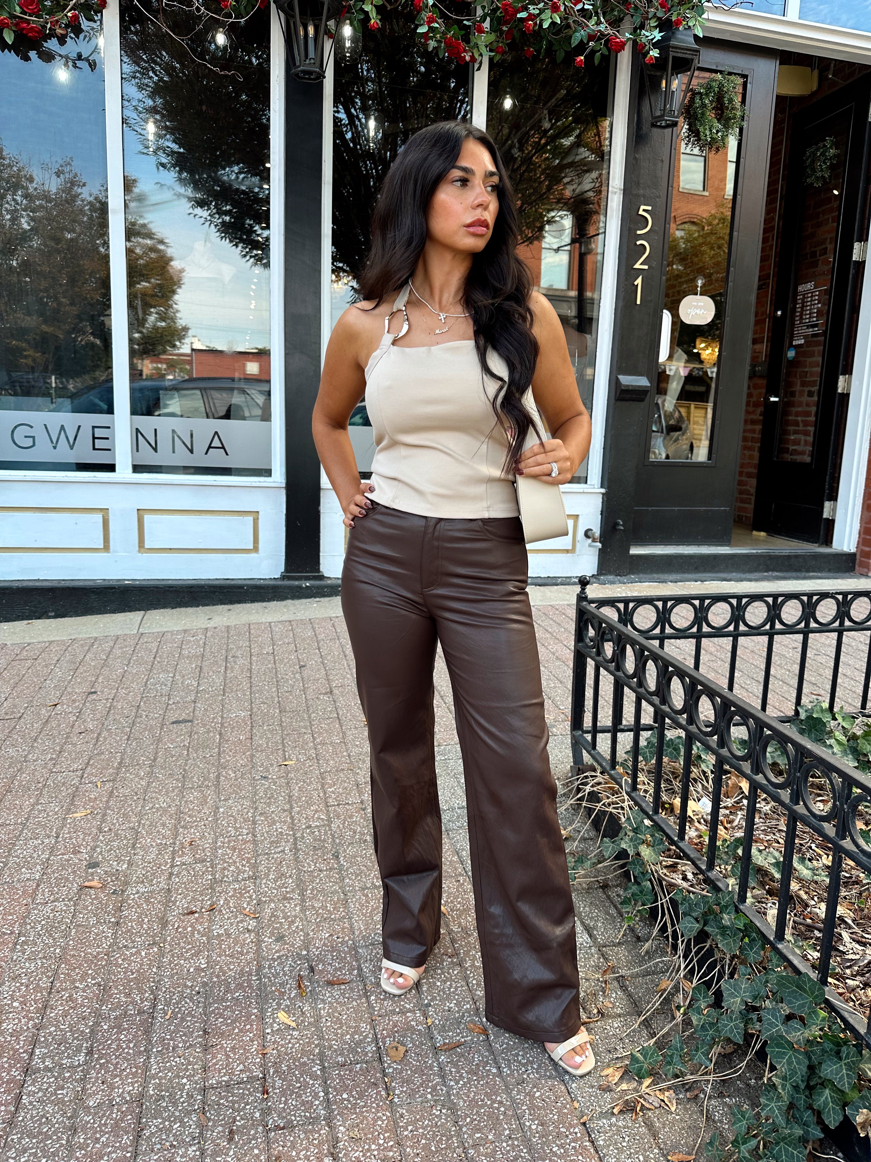 Woman wearing taupe halter neck top with chain link detail, and brown leather pant.