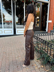 Woman wearing taupe halter neck top with chain link detail, and brown leather pant.
