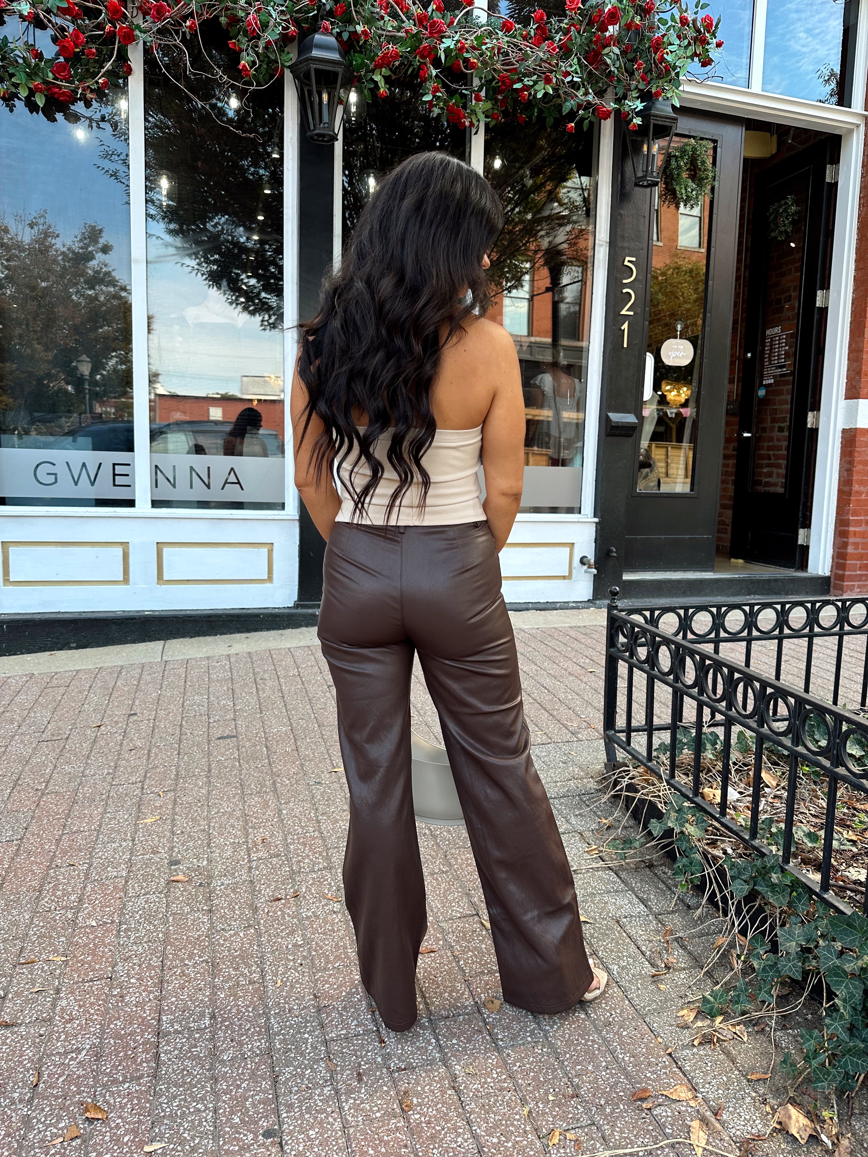 Woman wearing taupe halter neck top with chain link detail, and brown leather pant.