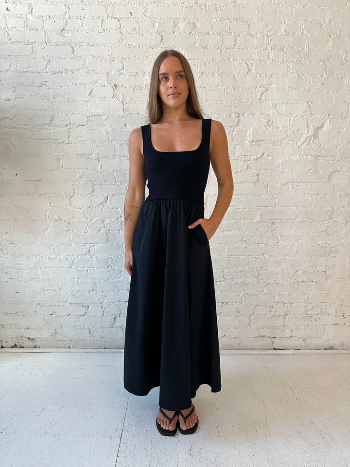 Woman wearing black midi dress with contrast knit top and flowy skirt with functional pockets.
