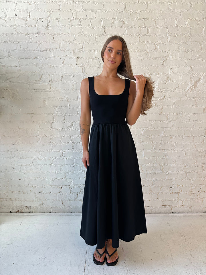 Woman wearing black midi dress with contrast knit top and flowy skirt with functional pockets.