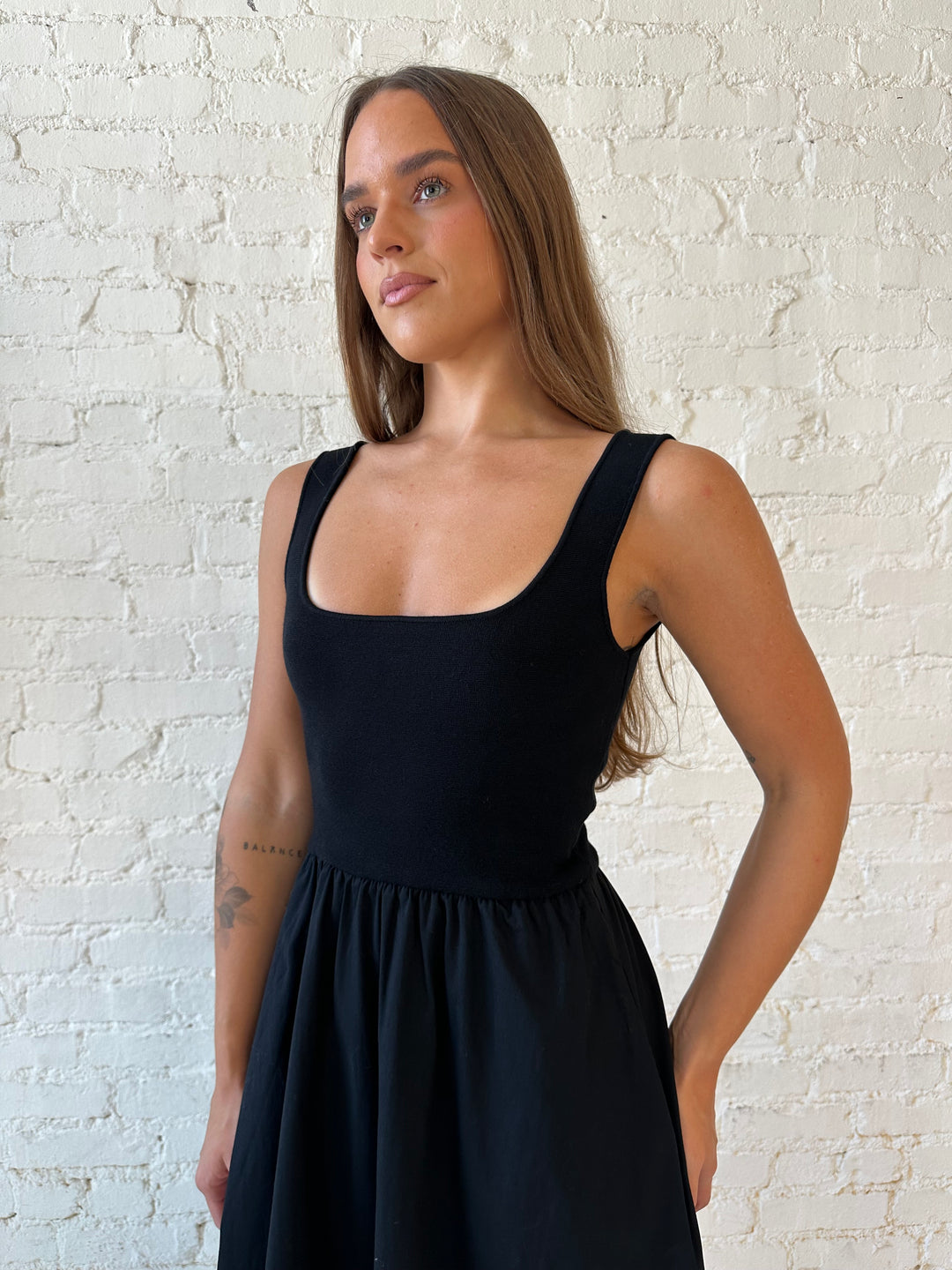 Woman wearing black midi dress with contrast knit top and flowy skirt with functional pockets.