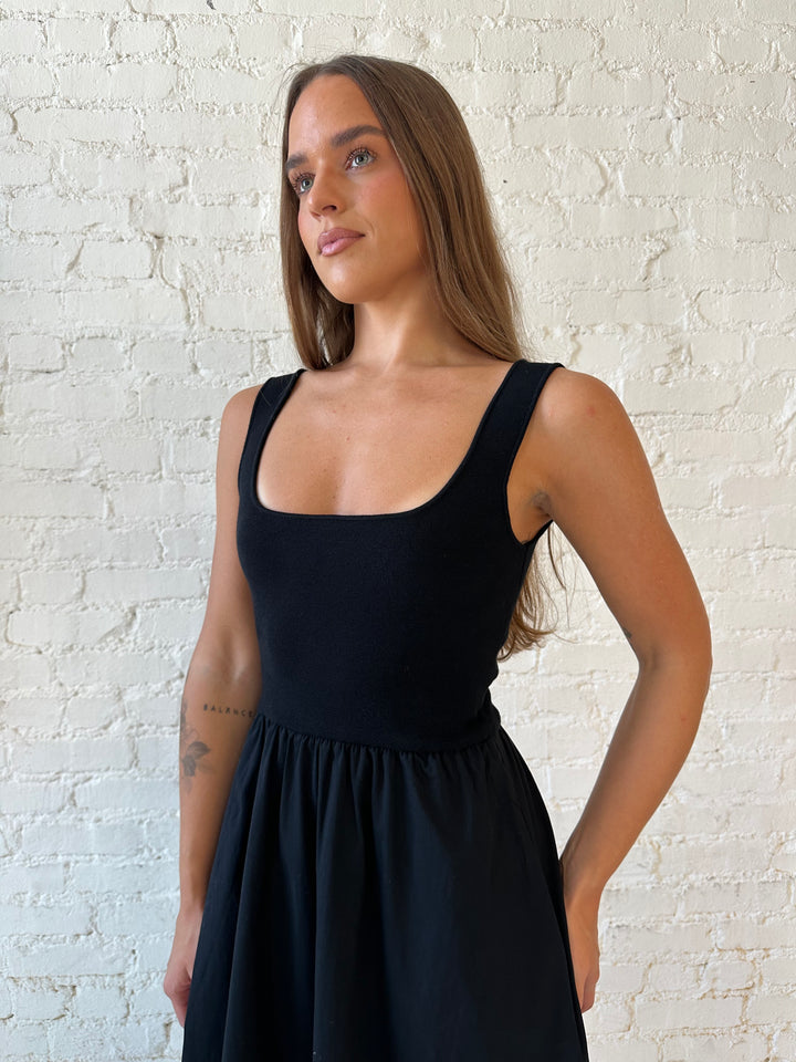 Woman wearing black midi dress with contrast knit top and flowy skirt with functional pockets.