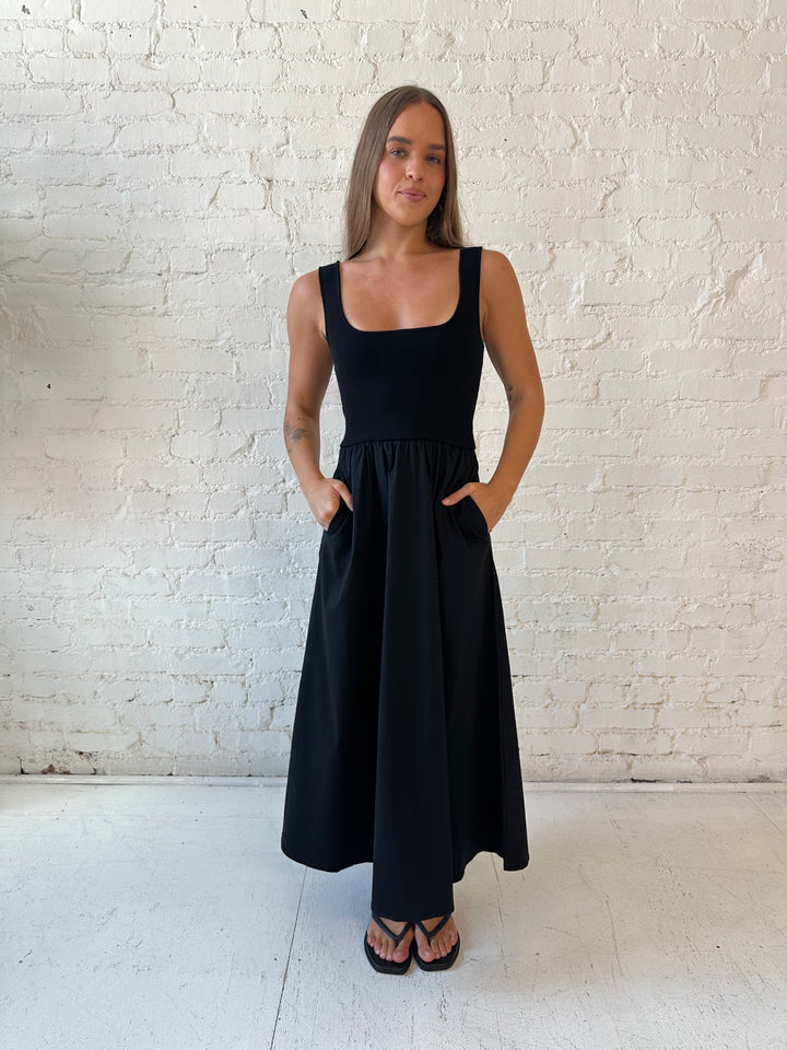 Woman wearing black midi dress with contrast knit top and flowy skirt with functional pockets.