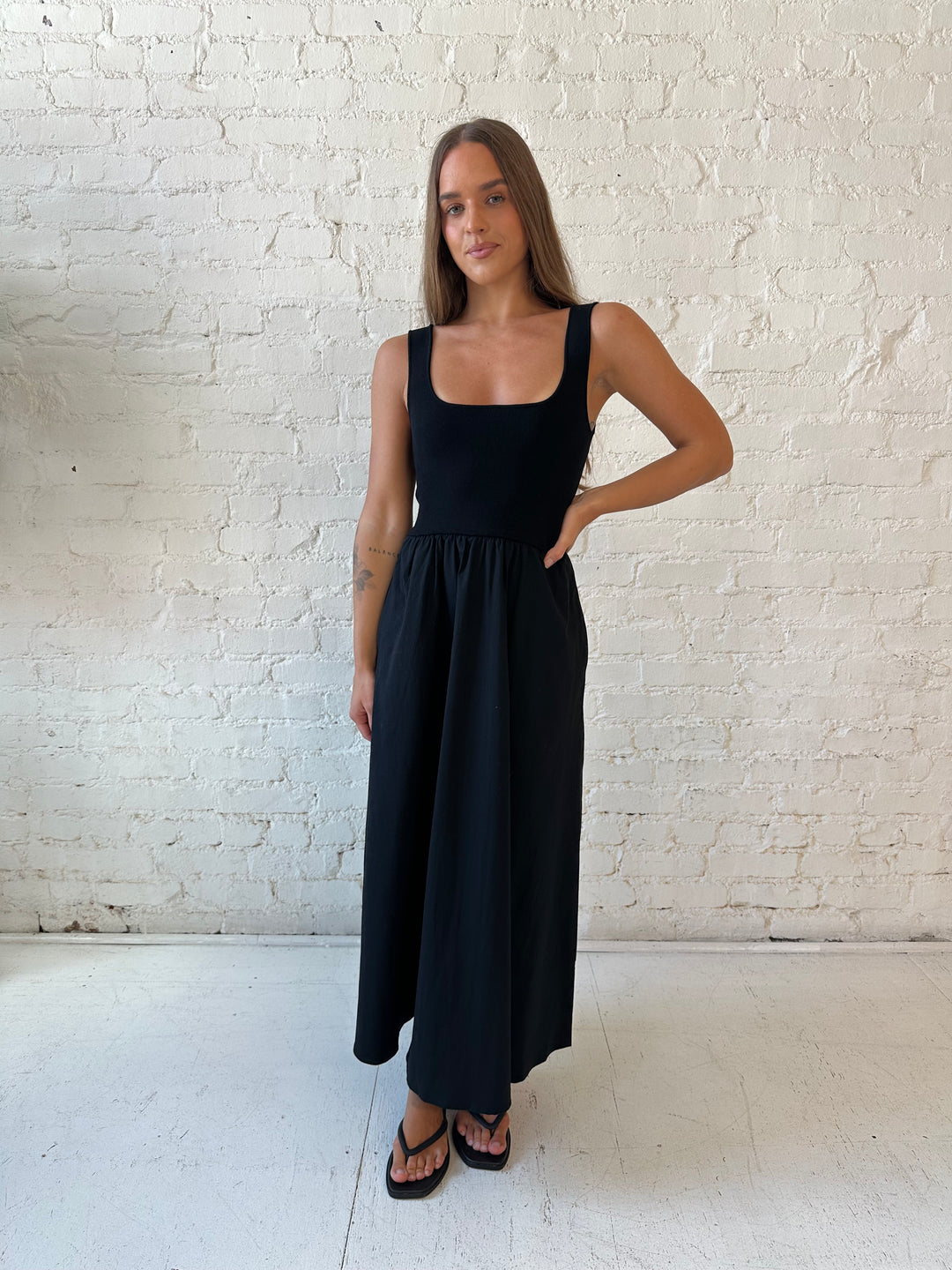 Woman wearing black midi dress with contrast knit top and flowy skirt with functional pockets.