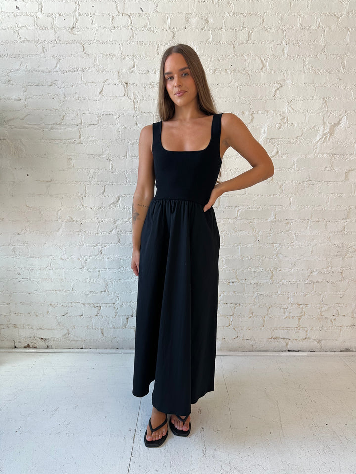 Woman wearing black midi dress with contrast knit top and flowy skirt with functional pockets.