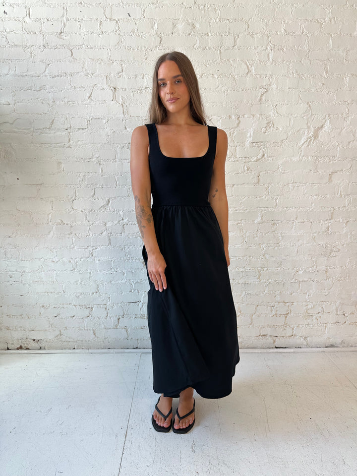 Woman wearing black midi dress with contrast knit top and flowy skirt with functional pockets.