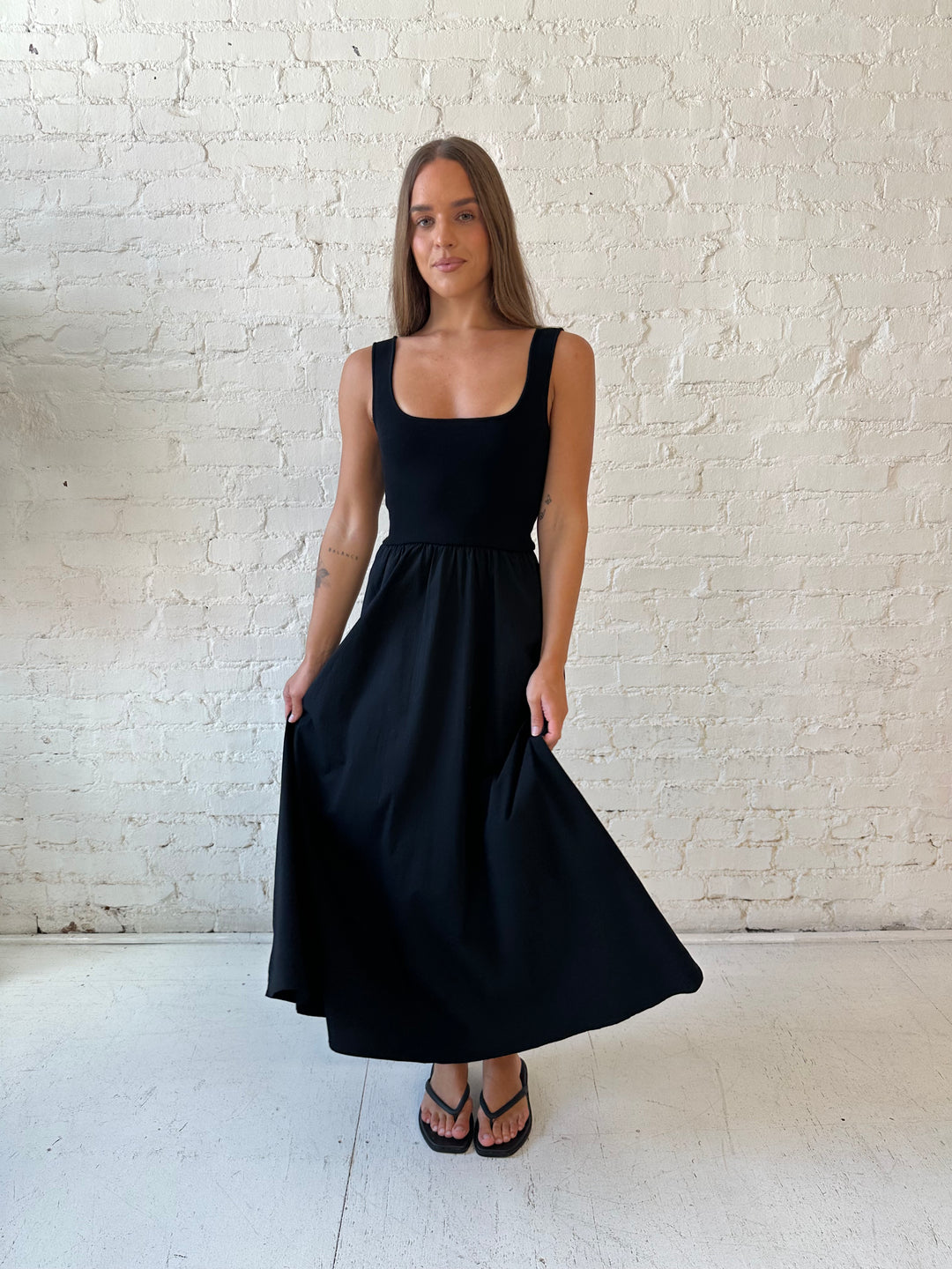 Woman wearing black midi dress with contrast knit top and flowy skirt with functional pockets.
