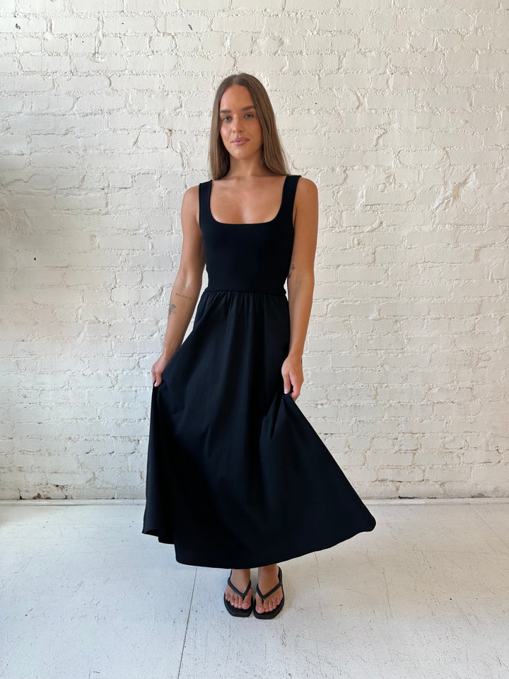Woman wearing black midi dress with contrast knit top and flowy skirt with functional pockets.