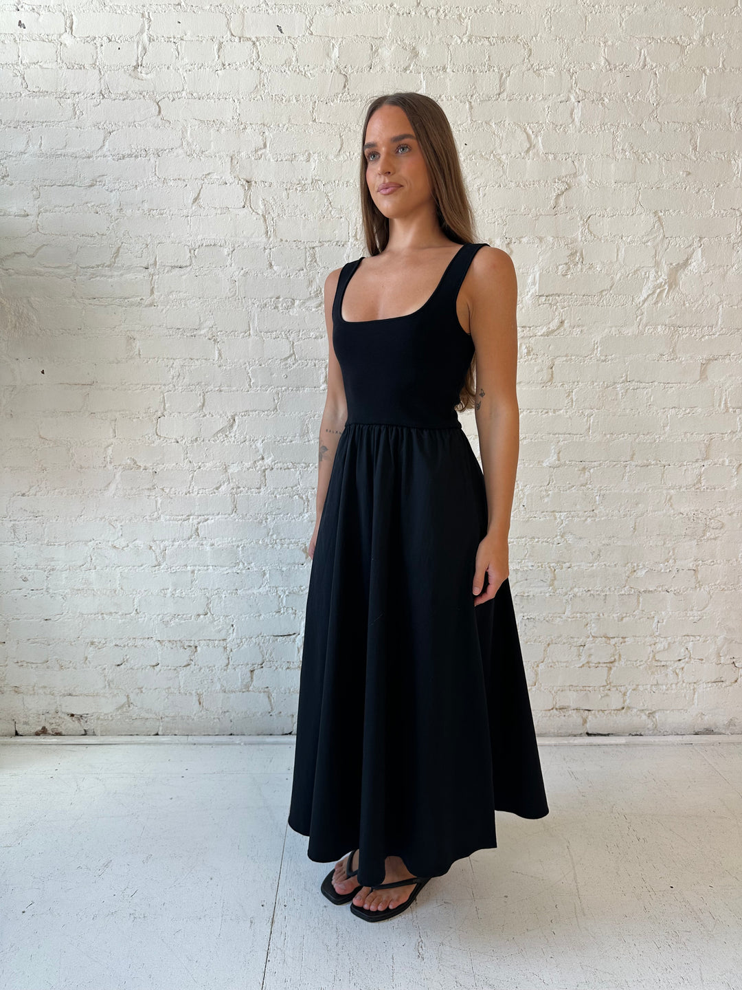 Woman wearing black midi dress with contrast knit top and flowy skirt with functional pockets.