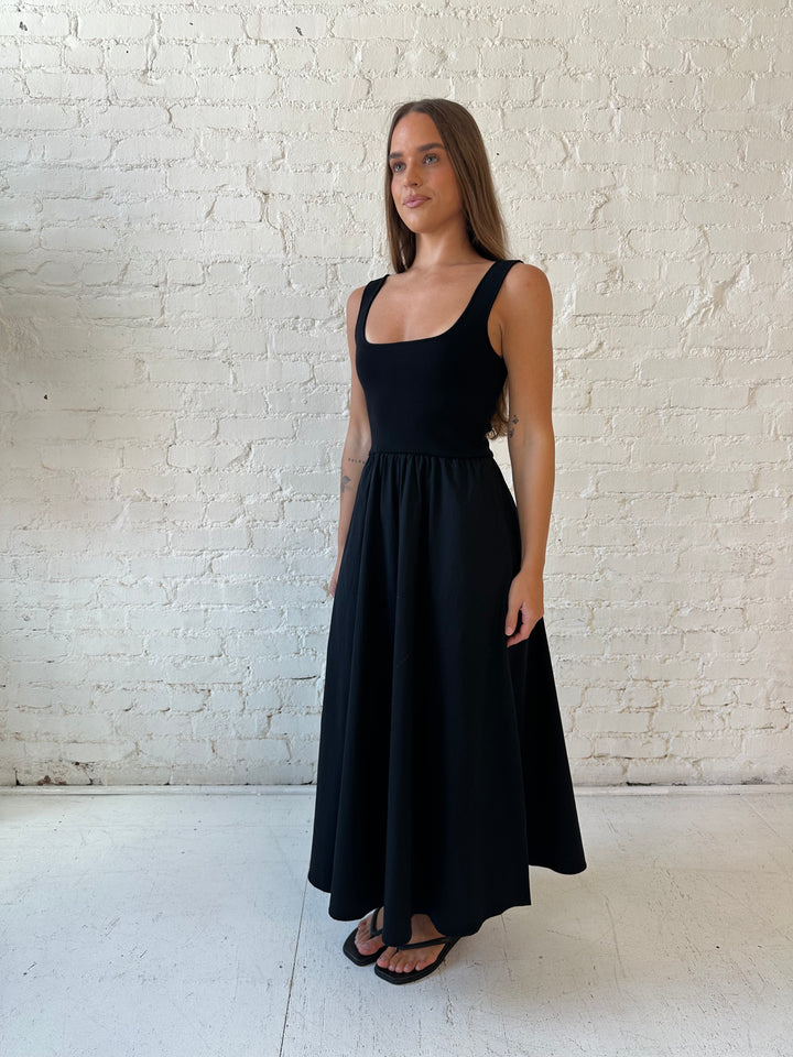 Woman wearing black midi dress with contrast knit top and flowy skirt with functional pockets.
