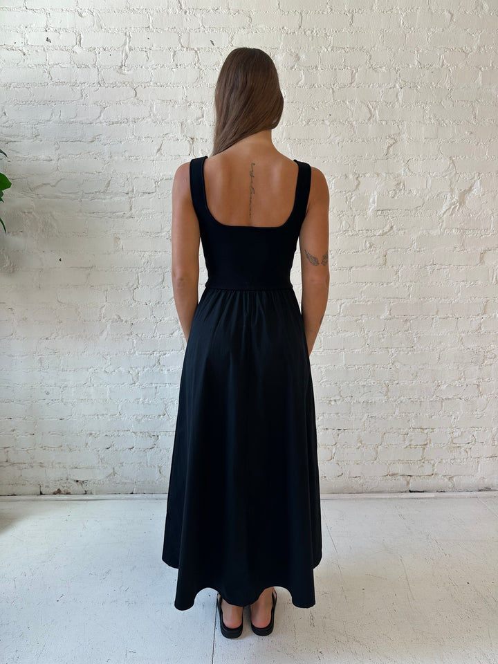Woman wearing black midi dress with contrast knit top and flowy skirt with functional pockets.