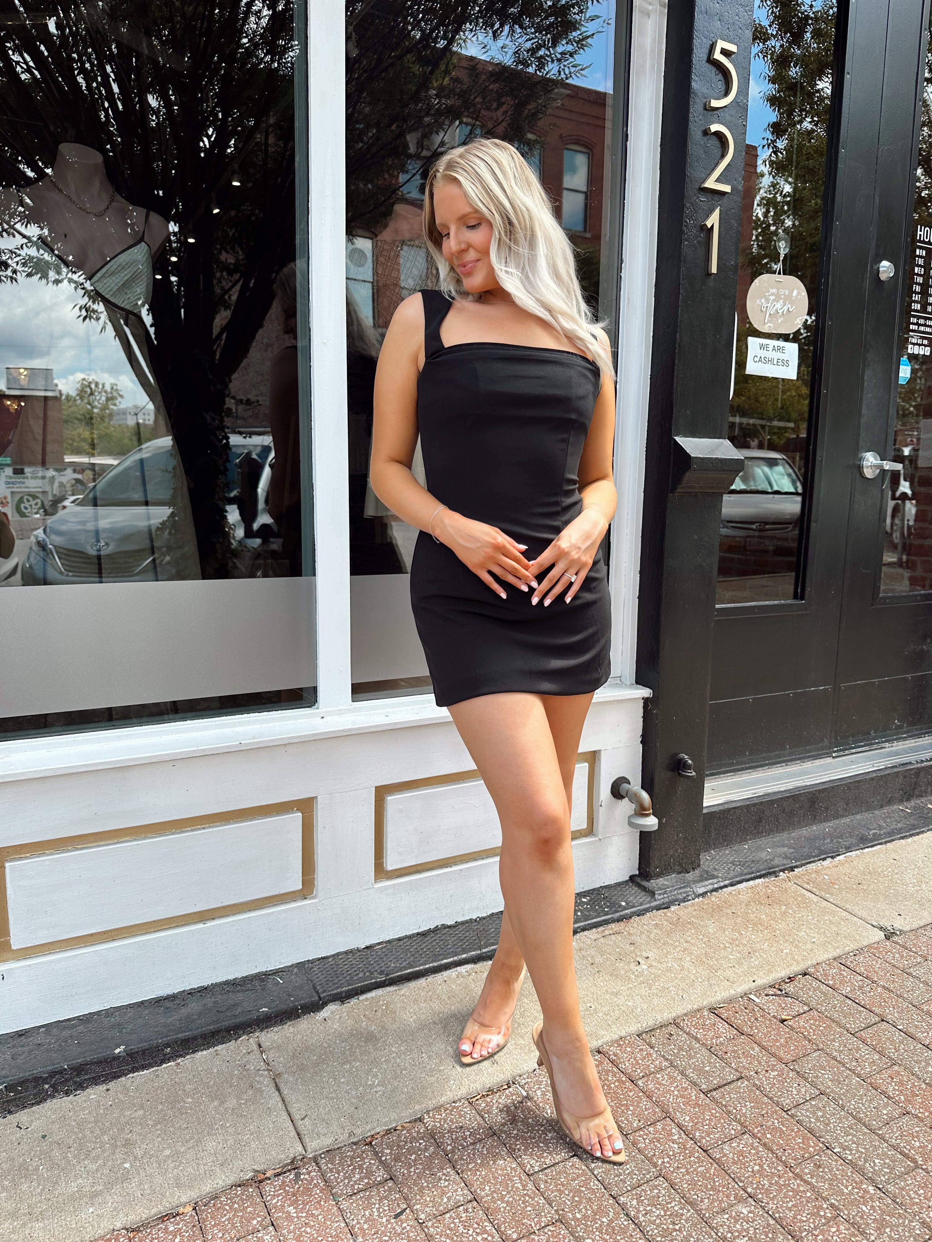 Woman wearing sleeveless black mini dress with square cowl neckline. 