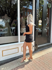 Woman wearing sleeveless black mini dress with square cowl neckline. 
