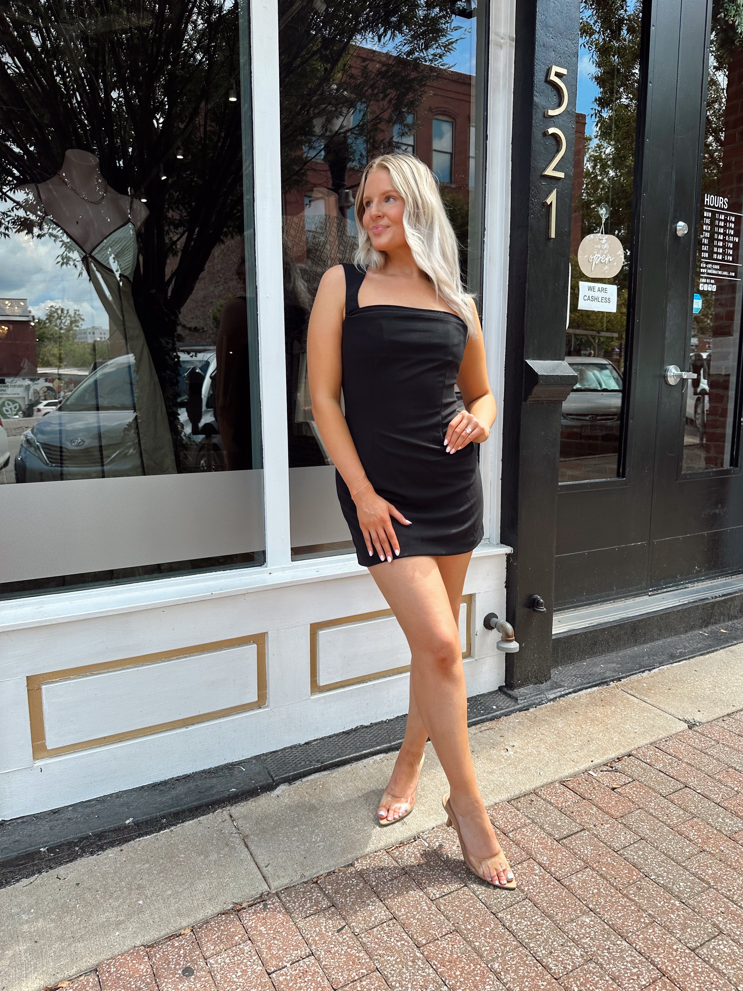 Woman wearing sleeveless black mini dress with square cowl neckline. 