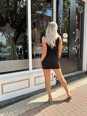Woman wearing sleeveless black mini dress with square cowl neckline. 