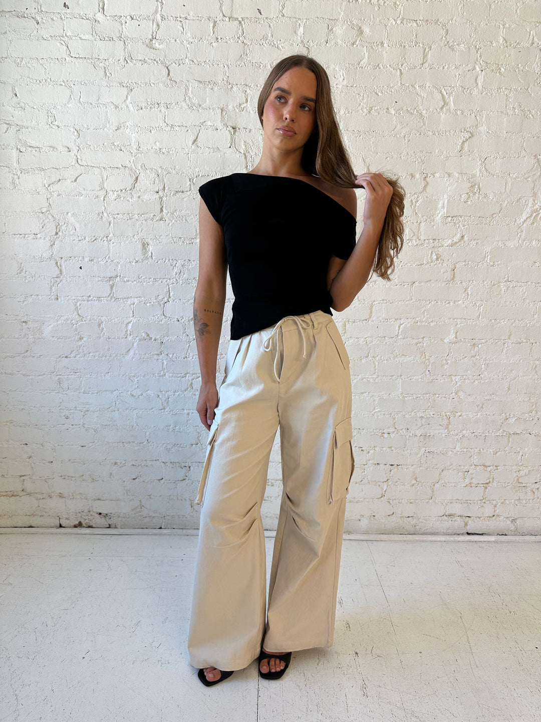 Woman wearing black knit off the shoulder top with khaki colored cargo pant. 