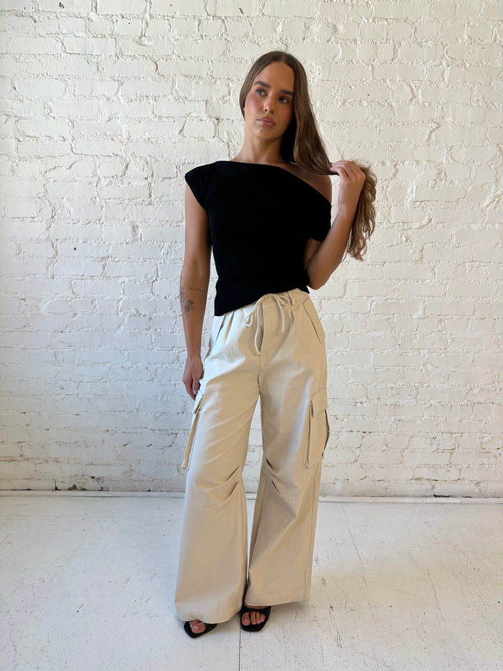 Woman wearing black knit off the shoulder top with khaki colored cargo pant. 