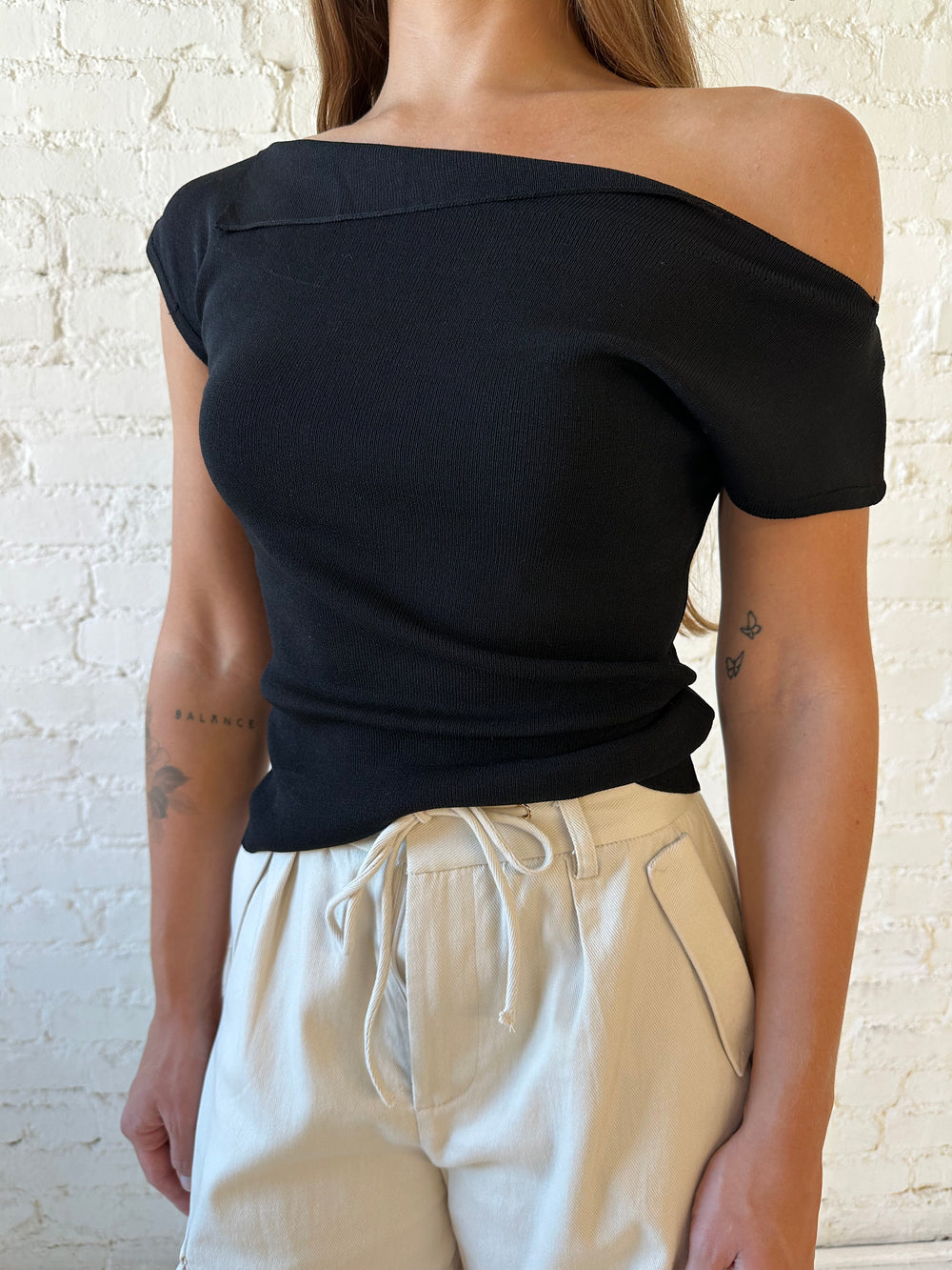 Woman wearing black knit off the shoulder top with khaki colored cargo pant. 
