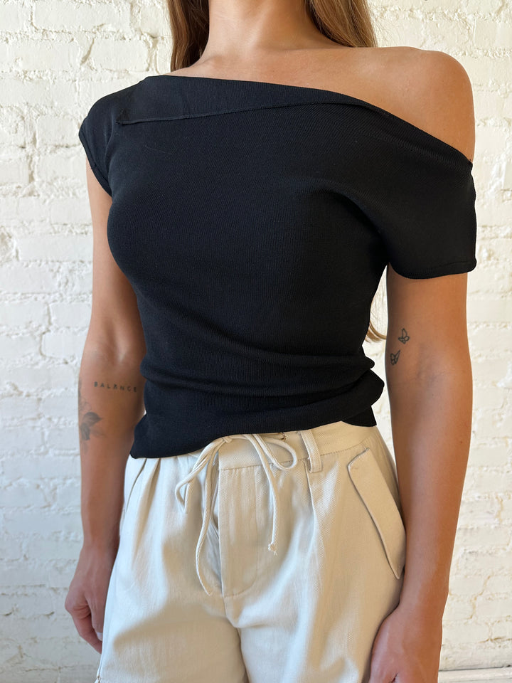 Woman wearing black knit off the shoulder top with khaki colored cargo pant. 