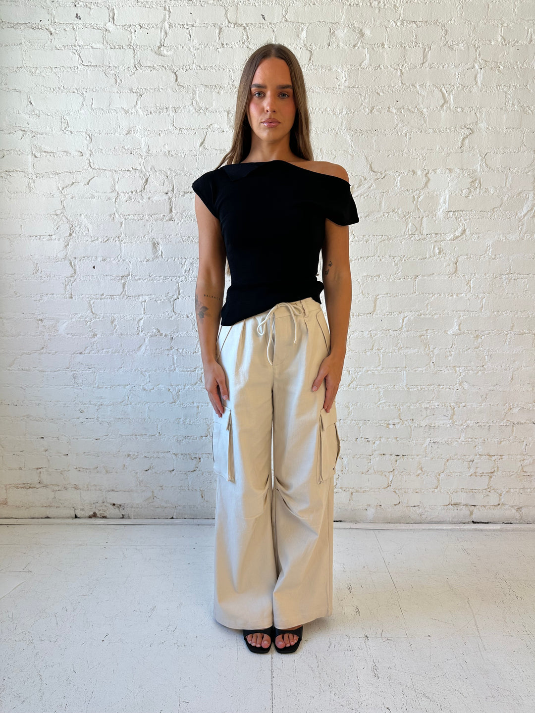 Woman wearing black knit off the shoulder top with khaki colored cargo pant. 