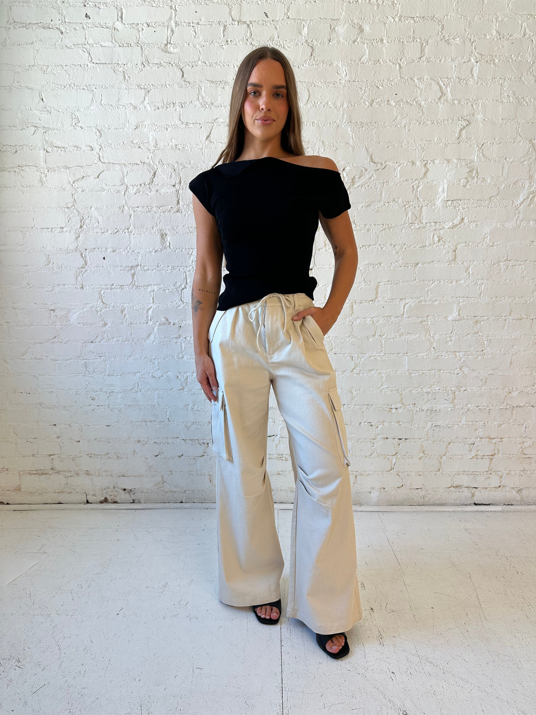 Woman wearing black knit off the shoulder top with khaki colored cargo pant. 
