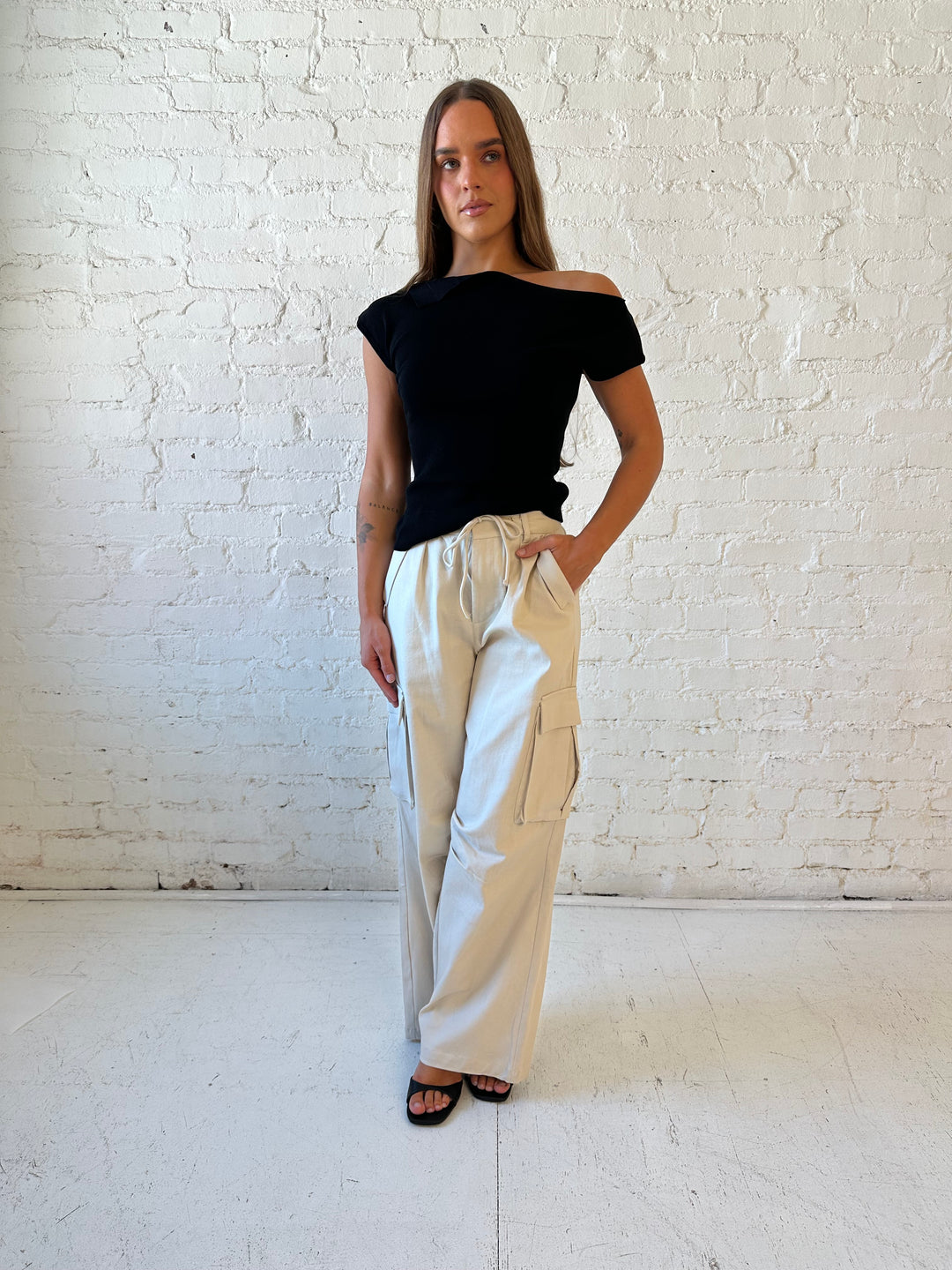 Woman wearing black knit off the shoulder top with khaki colored cargo pant. 