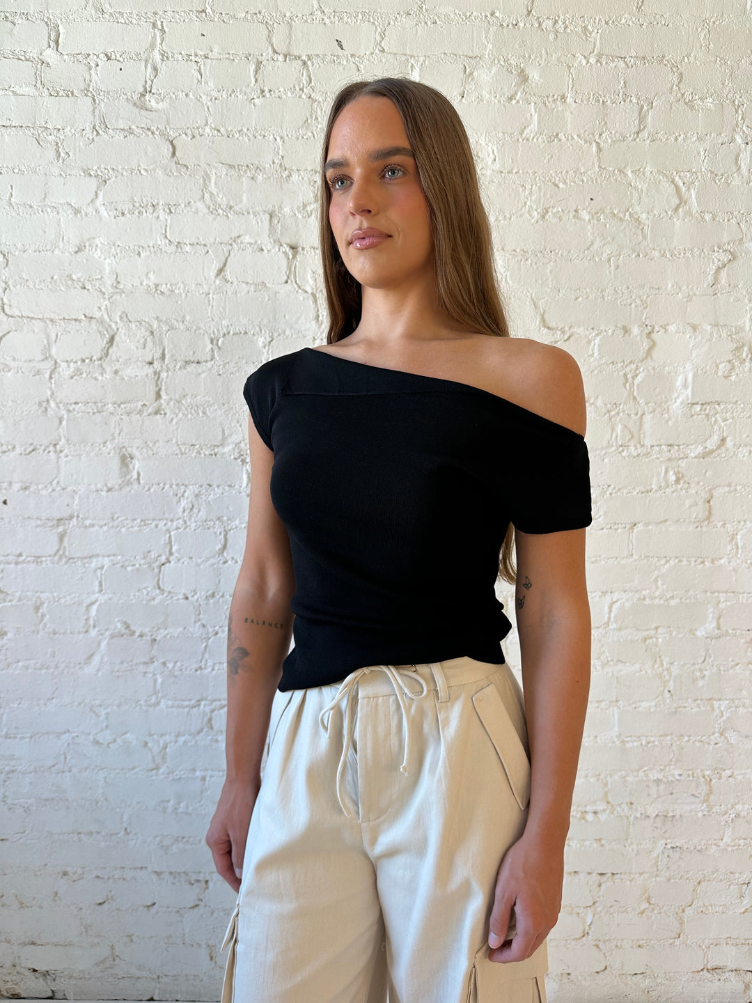 Woman wearing black knit off the shoulder top with khaki colored cargo pant. 
