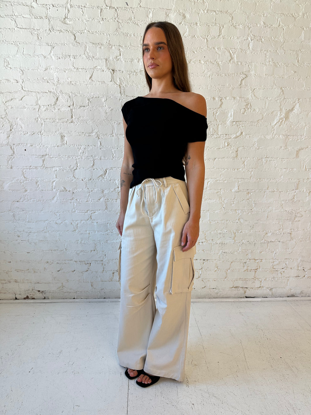 Woman wearing black knit off the shoulder top with khaki colored cargo pant. 