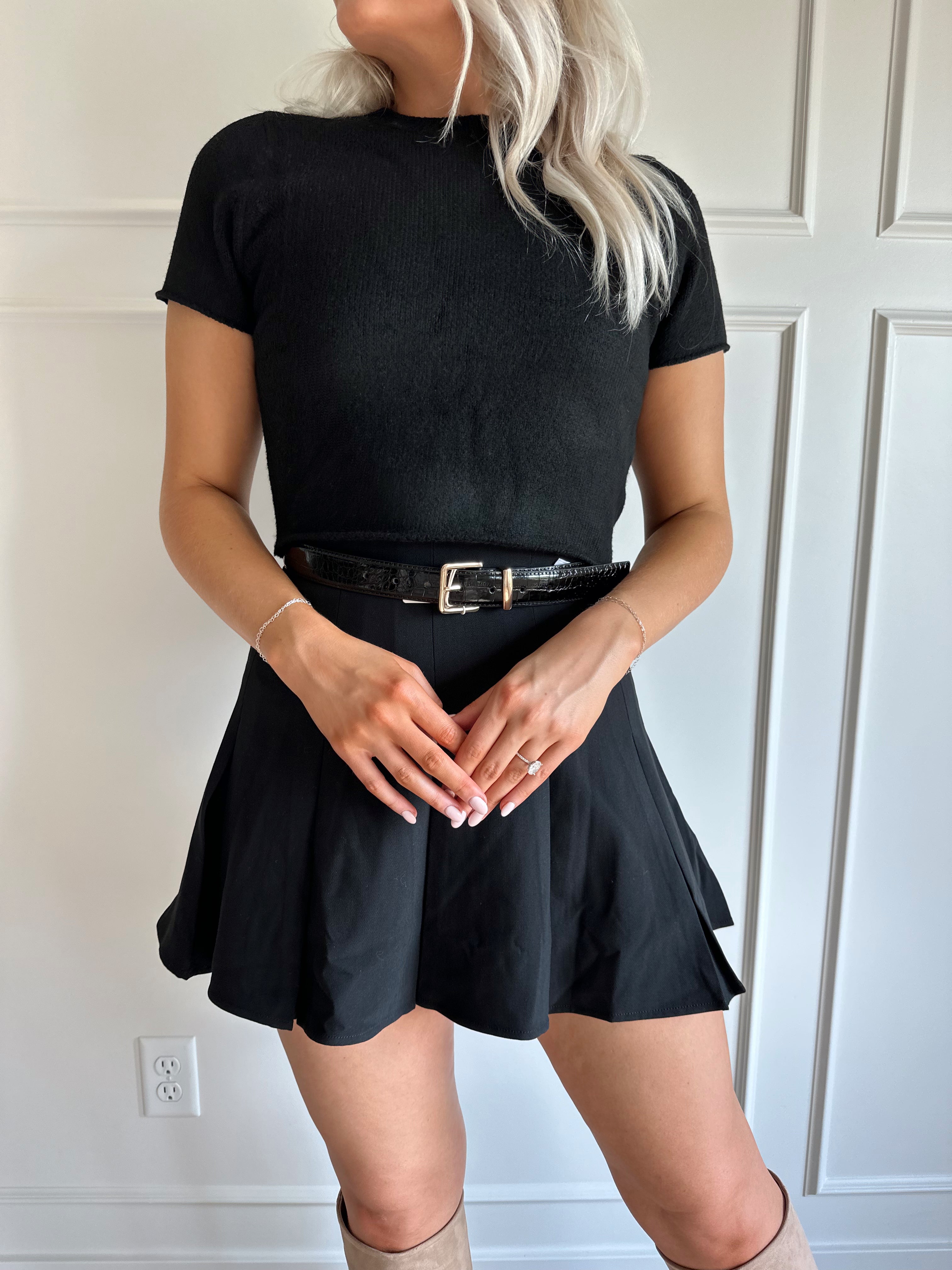 Woman wearing a black pleated mini skirt with black top and black croc belt.
