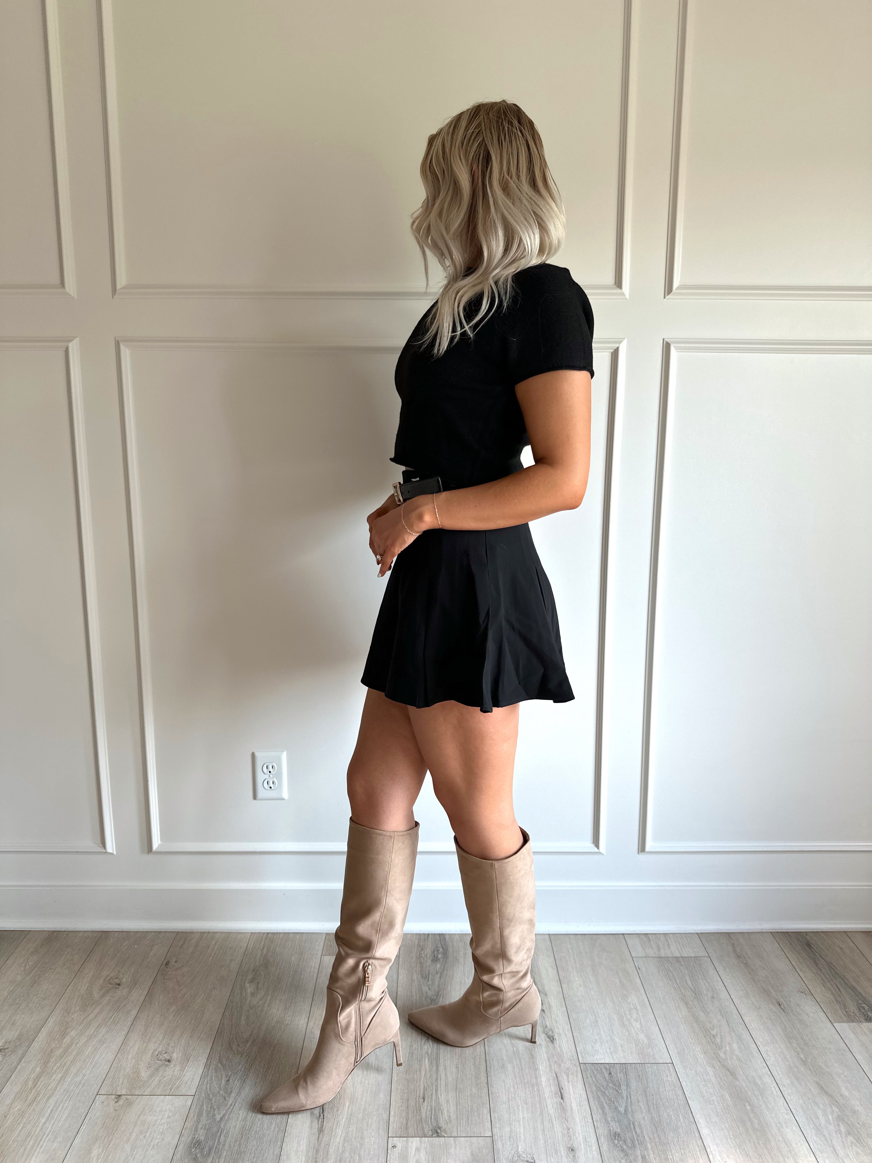 Woman wearing a black pleated mini skirt with black top and black croc belt.