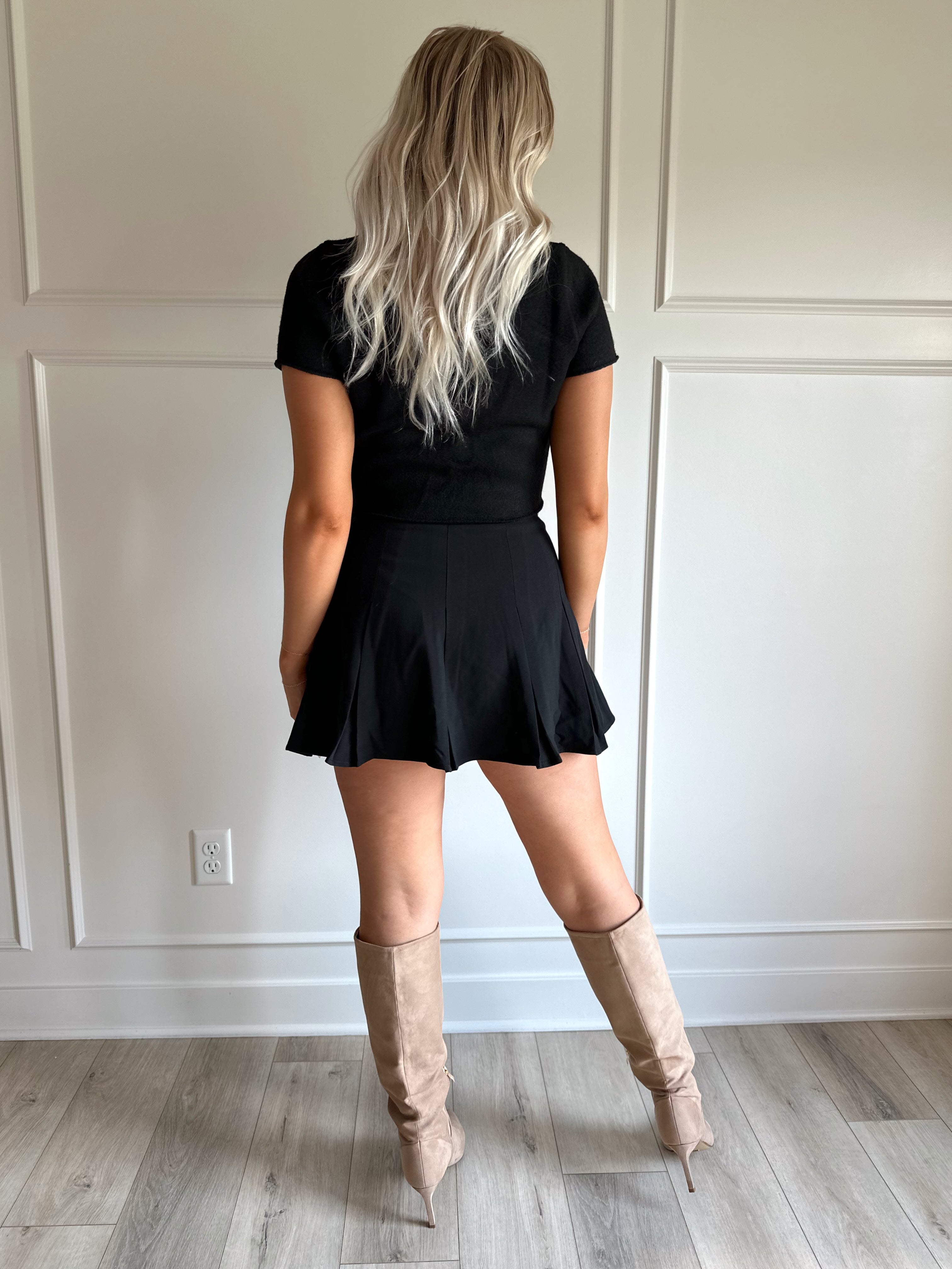 Woman wearing a black pleated mini skirt with black top and black croc belt.