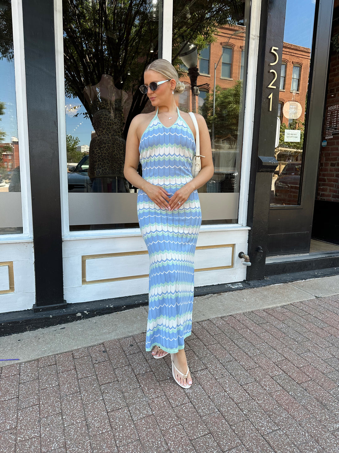 Woman wearing mint green. blue, and white chevron knit maxi dress with a halter neckline, and criss-cross open back. 