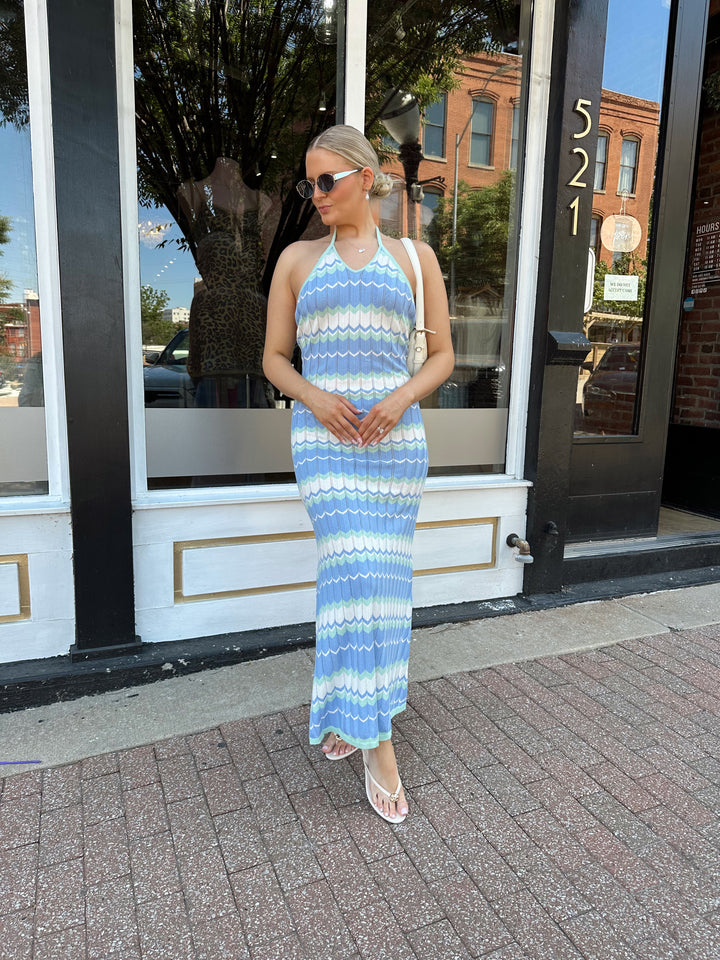 Woman wearing mint green. blue, and white chevron knit maxi dress with a halter neckline, and criss-cross open back. 