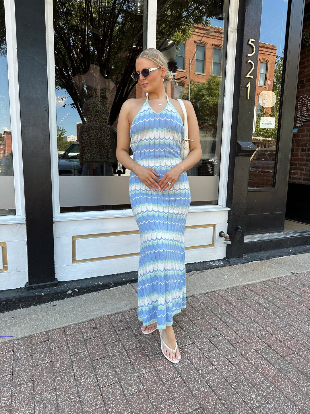 Woman wearing mint green. blue, and white chevron knit maxi dress with a halter neckline, and criss-cross open back. 