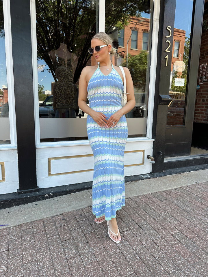 Woman wearing mint green. blue, and white chevron knit maxi dress with a halter neckline, and criss-cross open back. 