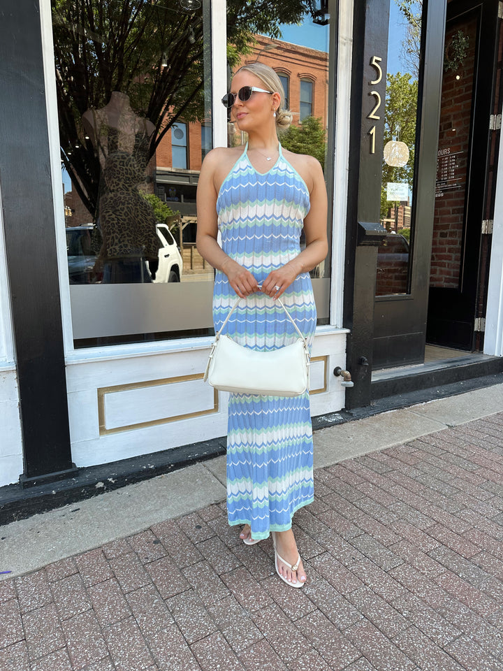 Woman wearing mint green. blue, and white chevron knit maxi dress with a halter neckline, and criss-cross open back. 