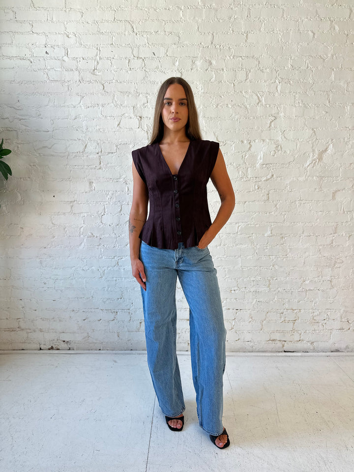 Woman wearing dark brown suede pleated peplum top with medium wash jeans. 