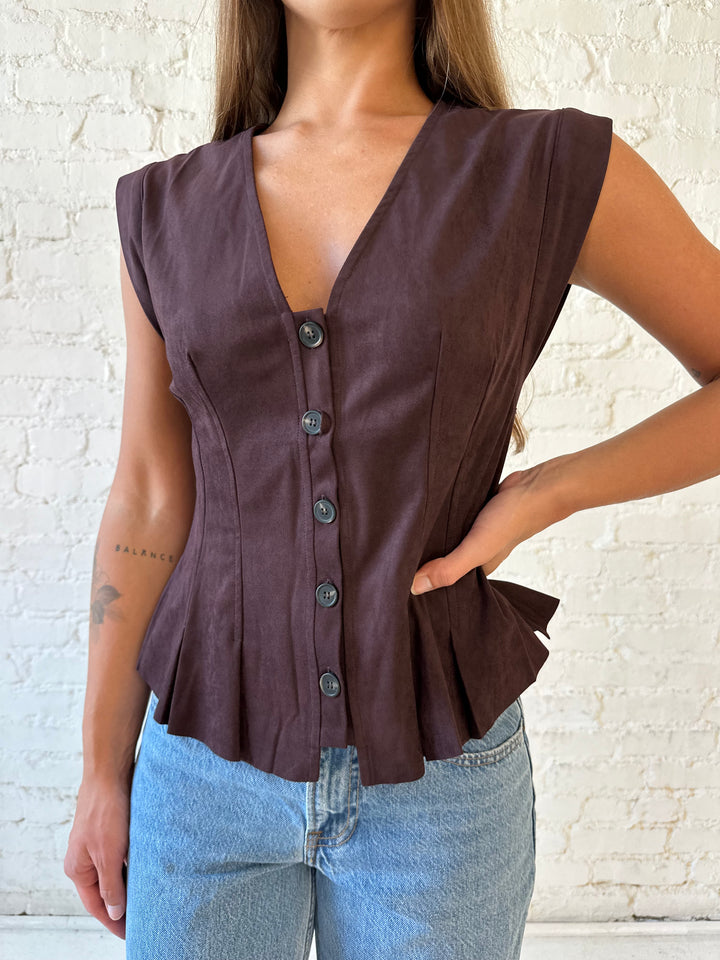 Woman wearing dark brown suede pleated peplum top with medium wash jeans. 
